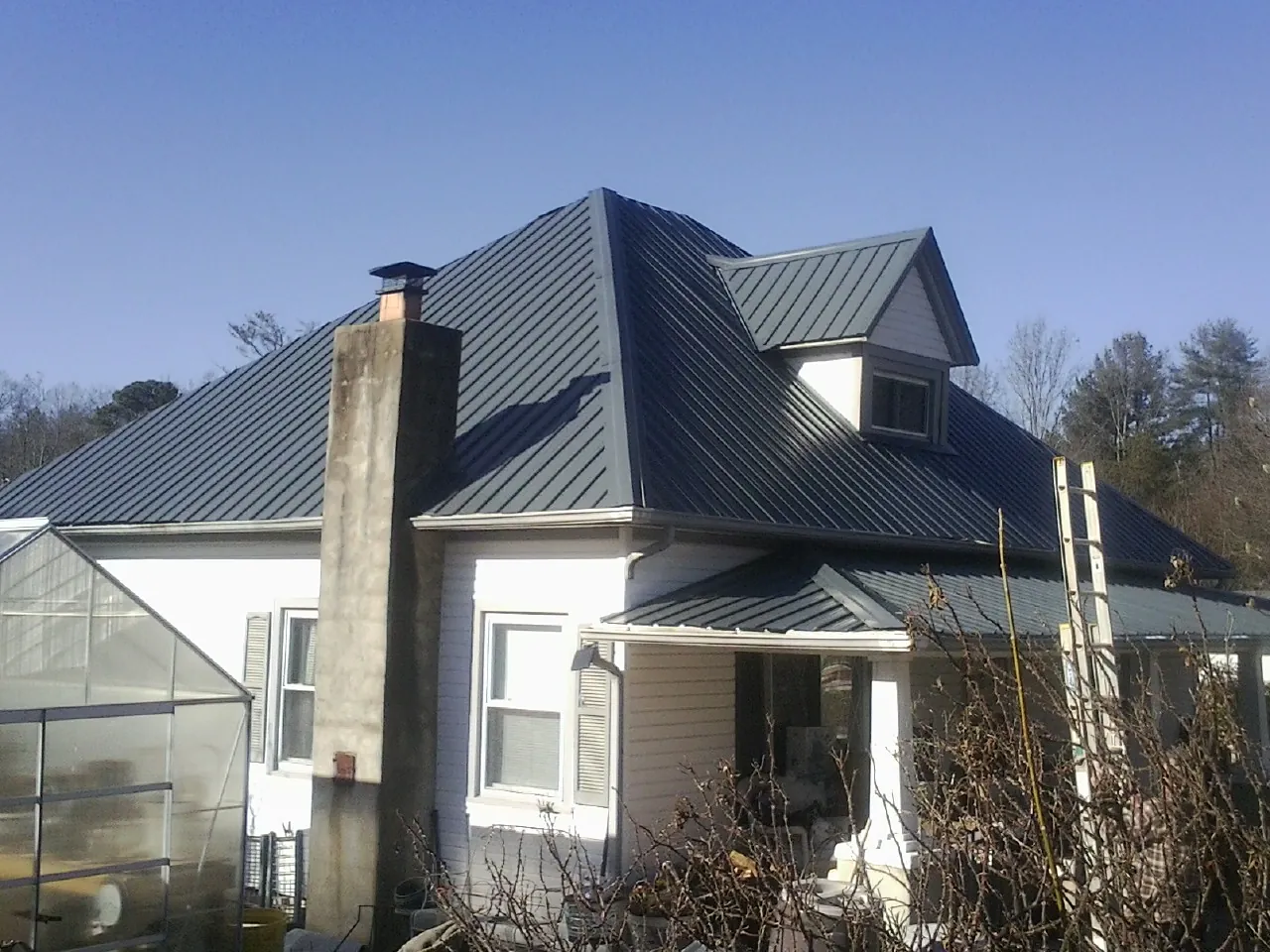 Dark blue standing seam metal roof on a white farmhouse with dormer — Slate & Tile Roof Repair by Roofing Brothers in Auburn Hills