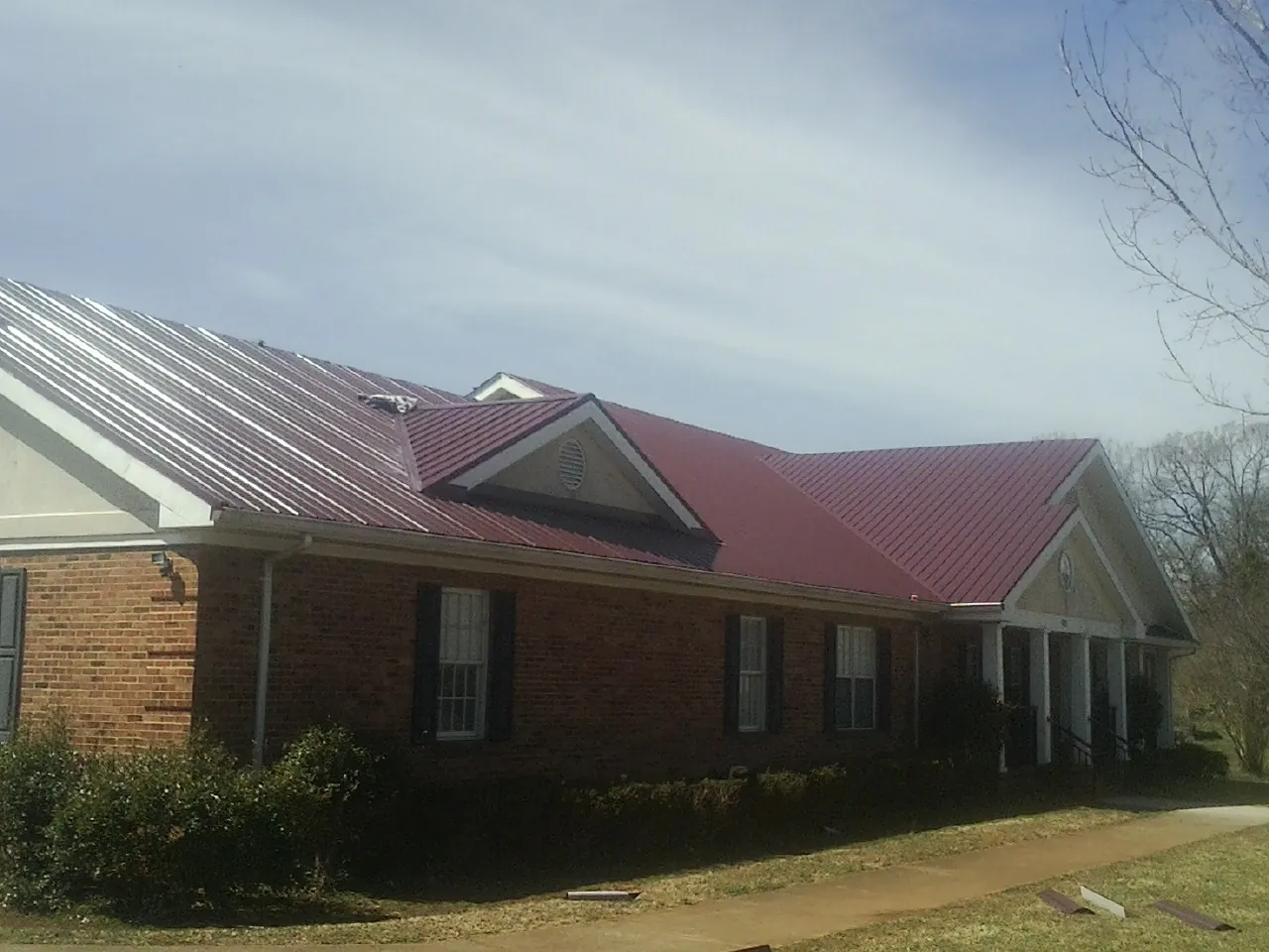 Red metal roof with gabled entries on a long brick building, from a Hail Damage Roof Repair job in Auburn Hills