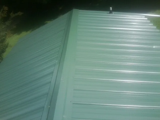 New green metal panels meeting at the ridge of a roof — Flat Roof Repair work by our crew in Auburn Hills