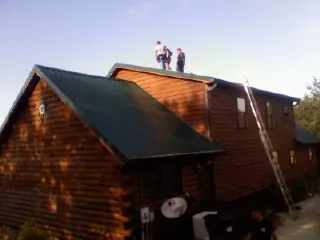 Crew on the ridge of a green metal roof on a two story log home in Auburn Hills