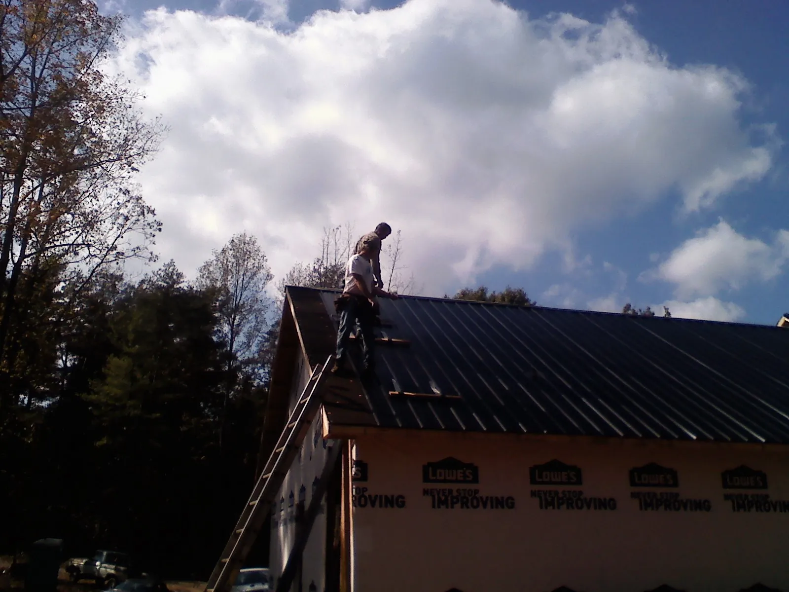 Roofer fastening dark metal panels high against a cloudy sky, from a Roof Inspection job in Auburn Hills
