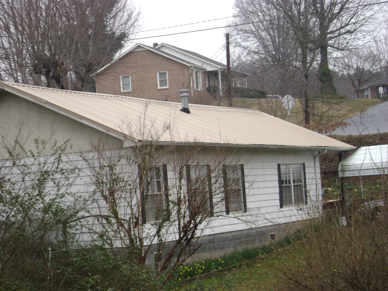 Tan metal roof on a white sided house set into a hillside — Commercial Roofing by Roofing Brothers in Auburn Hills
