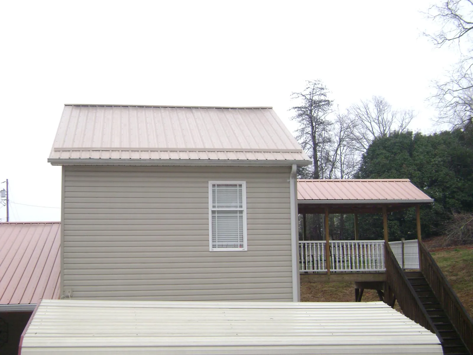 Tan metal roofs on a two story addition and attached porch, from a Roof Replacement job in Auburn Hills
